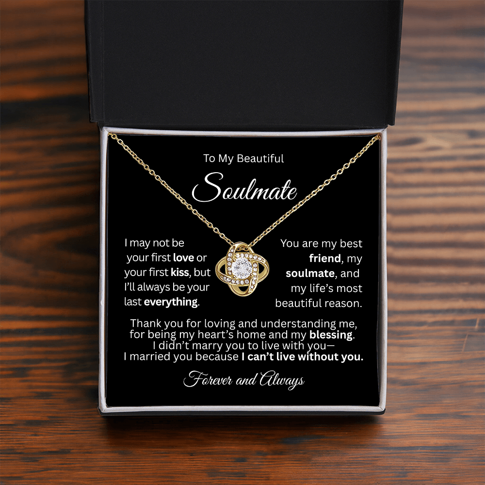 Gold love knot necklace in a red gift box with a heartfelt “To My Beautiful Soulmate” message card, on a brown table.