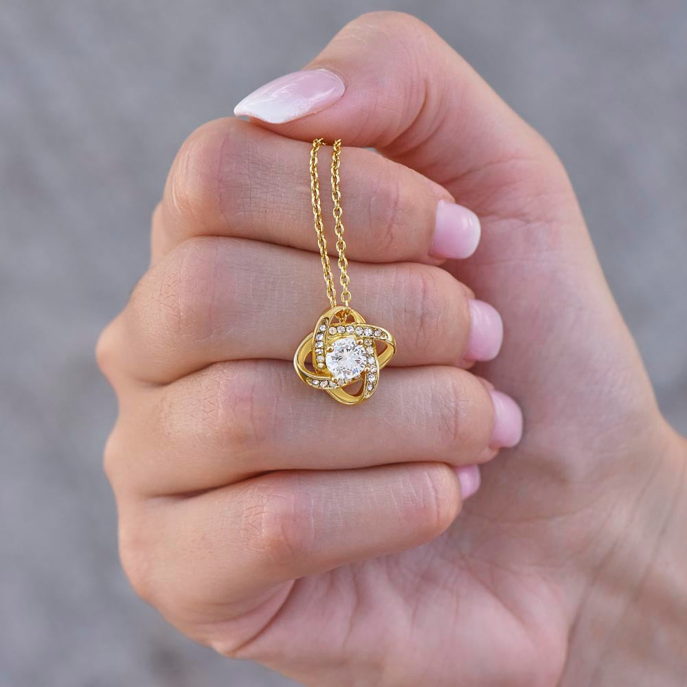 Gold love knot necklace held in a woman's hand.