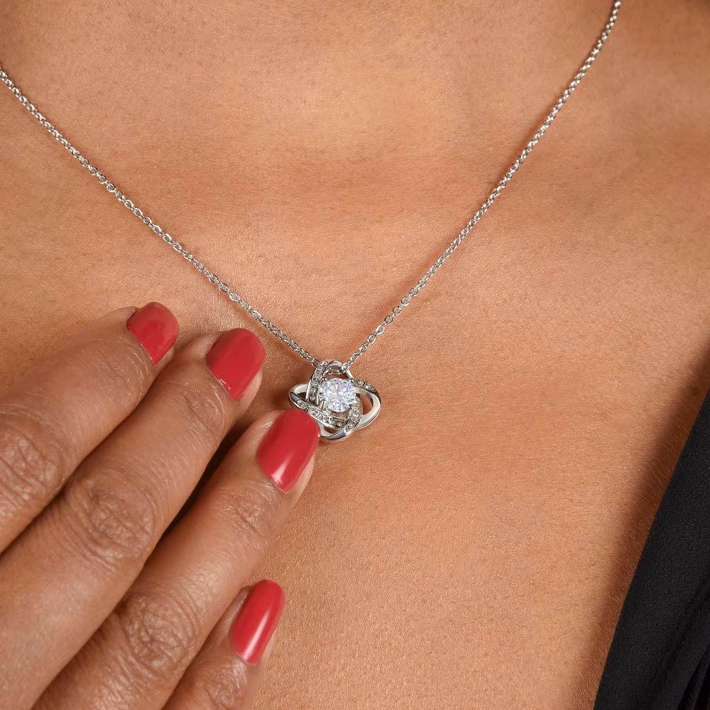 White gold love knot necklace around woman's neck.